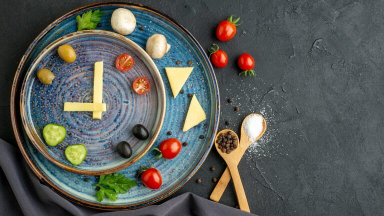 Ein kreativ angerichteter Teller mit Gemüse, Käse und Gewürzen in Form einer Uhr auf blauem Geschirr.