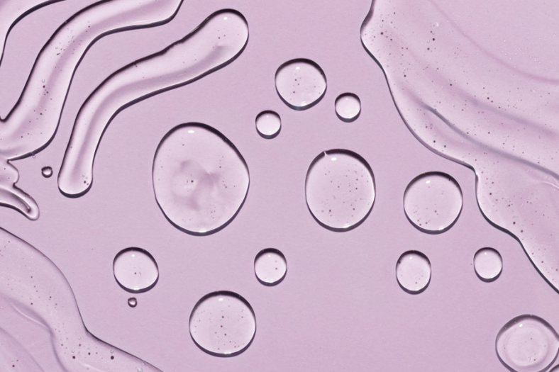 Transparente Wassertropfen auf einem helllila Hintergrund, mit fließenden Linien und Blasen.