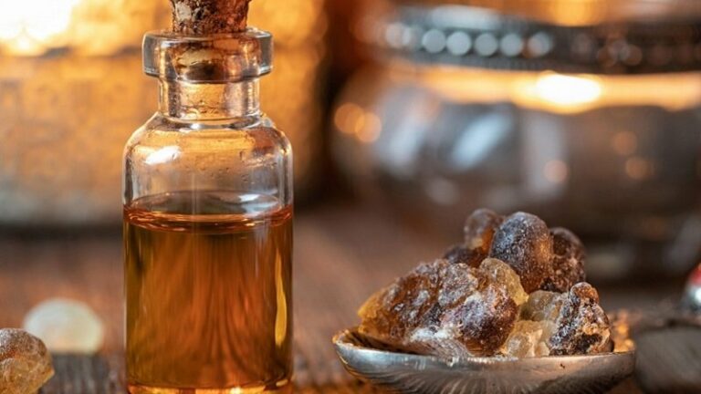 Ein Glasfläschchen mit Korken, gefüllt mit goldbraunem Öl, neben einem silbernen Teller mit Harzstücken.