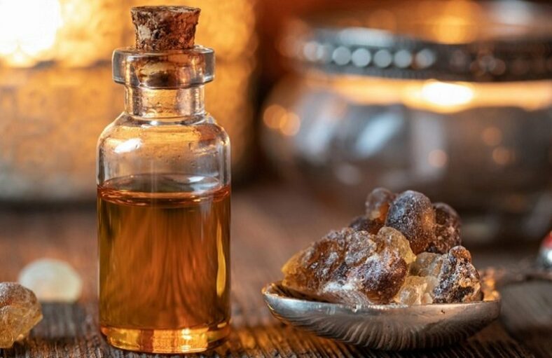 Ein Glasfläschchen mit Korken, gefüllt mit goldbraunem Öl, neben einem silbernen Teller mit Harzstücken.